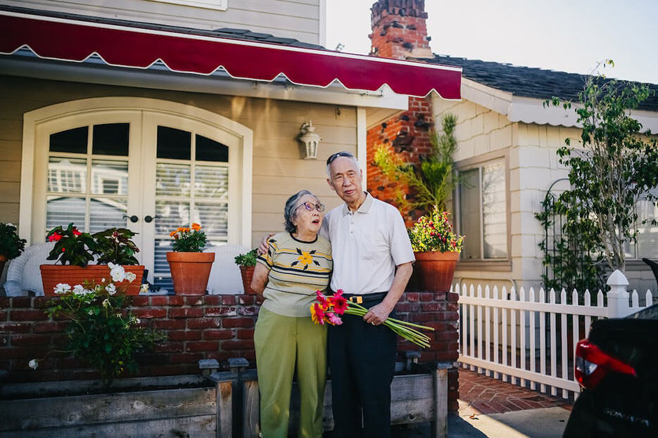 senior couple standing behind their home