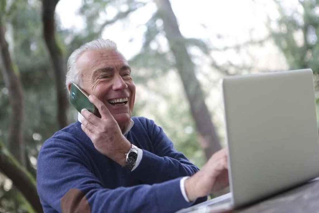 man in blue sweater using cell phone and laptop