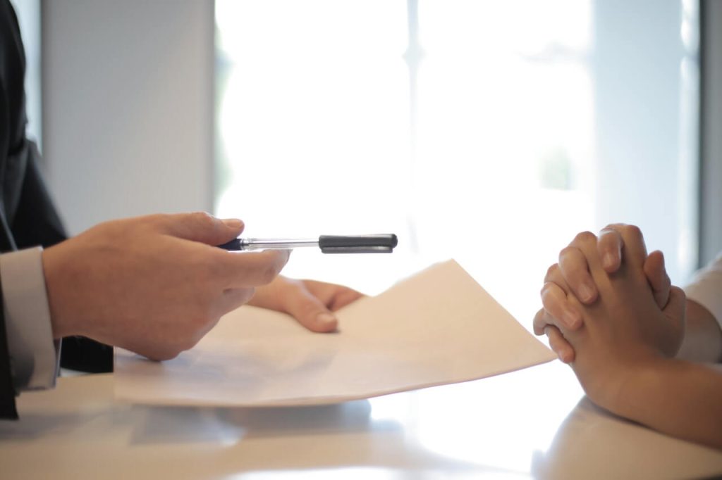 hands handing over pen and contract