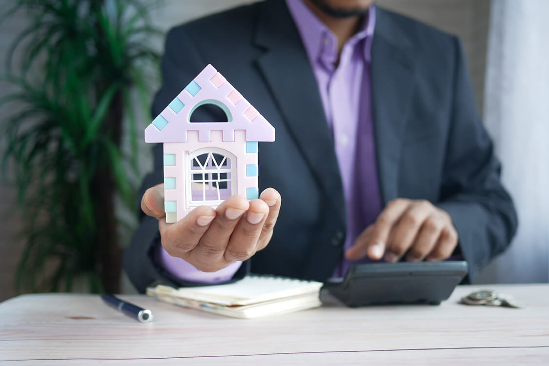 mortgage broker with pink and lavender house figurine in hand