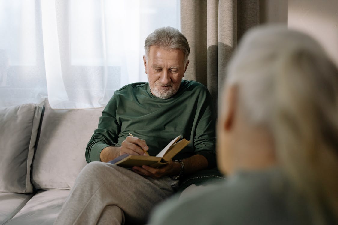elderly man reading book on couch across from woman